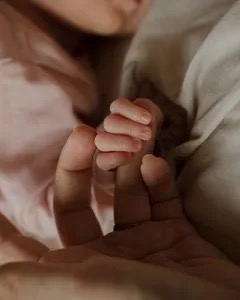 Tender candid moment of a young loving mother gently kissing her newborn baby's forehead in a bright sunlit bedroom at home