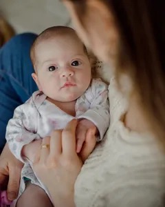 Cute smiling six month old baby sitting on cozy knitted neutral blanket with natural wooden toy